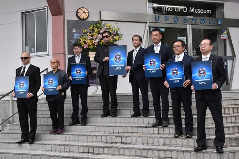 Primeiros associados ao International UFO Lab segurando um cartaz com a insígnia da instituição durante cerimônia de inauguração
