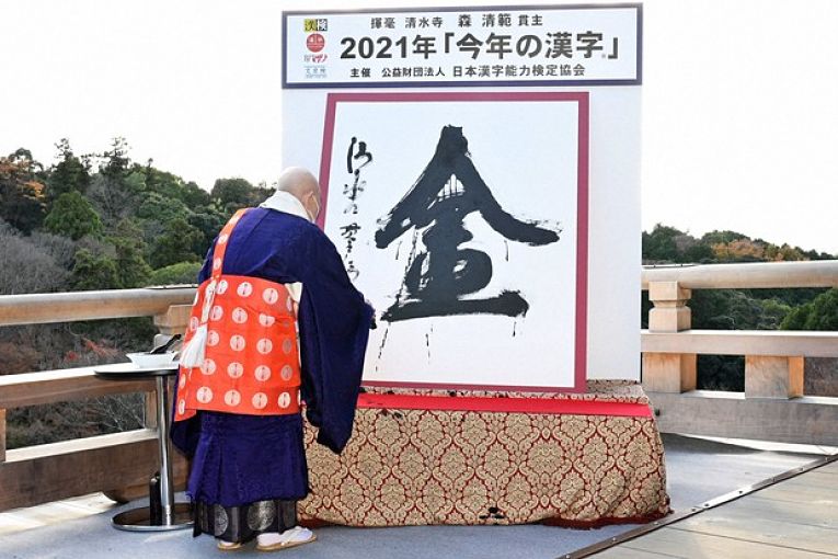 Monge Seihan Muri escrevendo com pincel pequeno o significado do kanji Kin (金)