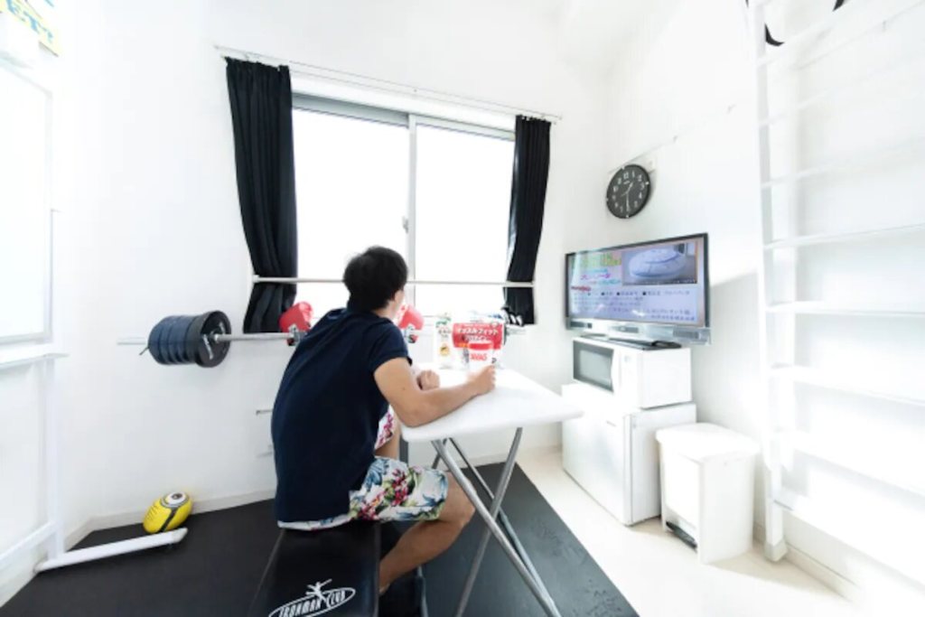 Homem senta e assiste televisão na sala de seu microapartamento no Japão
