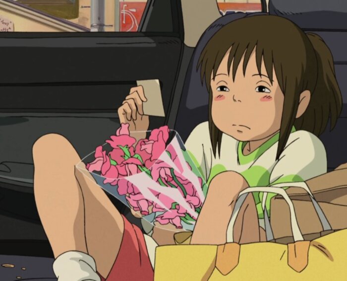 Chihiro em cena da animação A viagem de Chihiro em que olha com tédio o presente de seu pai (flores)