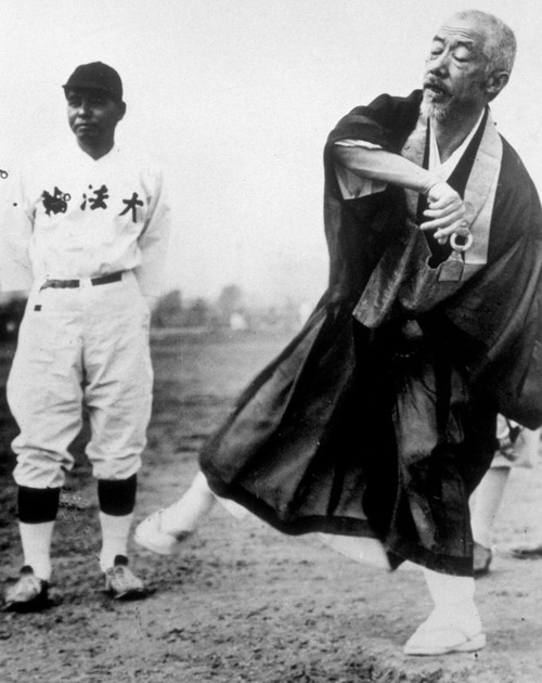 Monge budista jogando baseball em meados de 1935. Diferente dos esportes de contato, o baseball exige grande foco e concentração para além da força física, caracterísitcas que vão de encontro com a tradição das artes marciais do Japão
