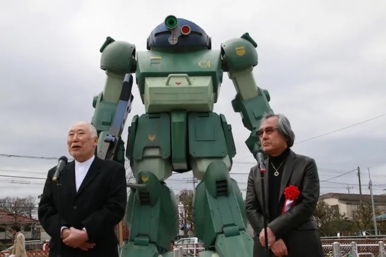 O diretor do anime Armored Trooper VOTOMS, Ryosuke Takahashi (esquerda), e o designer dos VOTOMS, Kunio Okawara (direita) durante a inauguração de um VOTOMS no Inagi Pear Park na cidade de Inagi, provínciade Tokyo em 2020